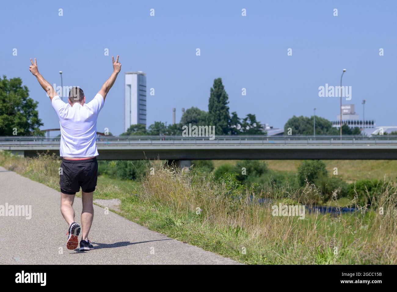 Gros plan d'un homme expérimenté qui s'éloigne de la caméra, faisant un panneau en V le long d'un sentier le long d'un canal lors d'une journée d'été ensoleillée Banque D'Images