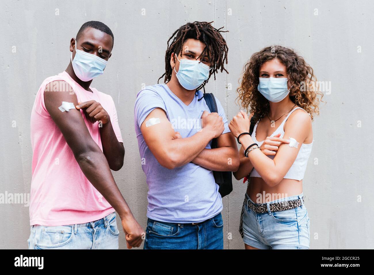 amis africains, latino-américains et caucasiens montrant des armes avec un morceau de coton. Concept du programme de vaccination Covid Banque D'Images