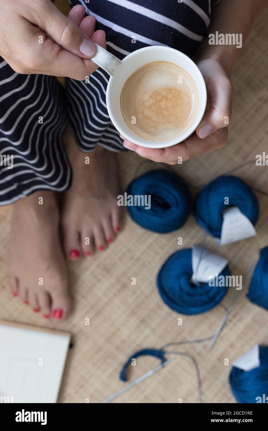 Vue aérienne d'une femme assise en robe rayée montrant une tasse de café sur un fond en crochet flou. Banque D'Images