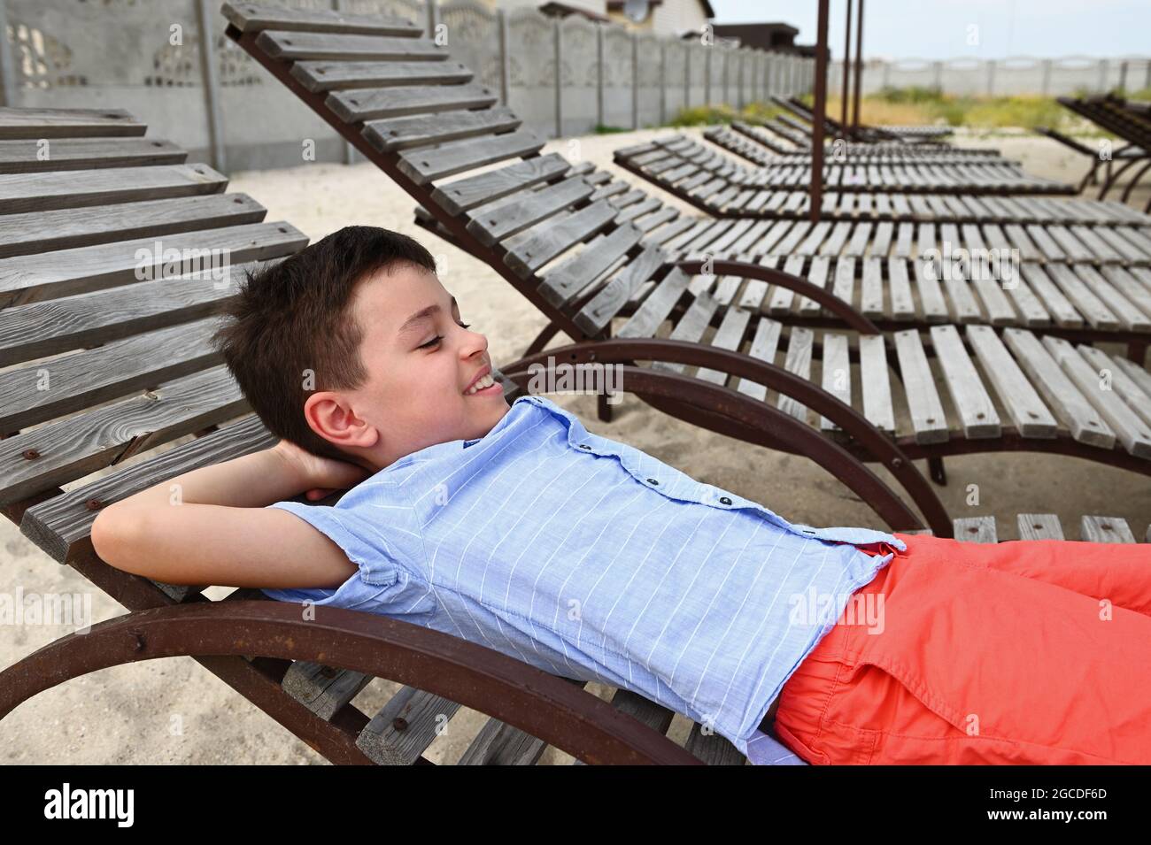 Joyeux adolescent allongé sur une chaise longue en bois. Beau enfant qui se  repose sur la chaise longue pendant les vacances d'été. Les enfants en  vacances Photo Stock - Alamy