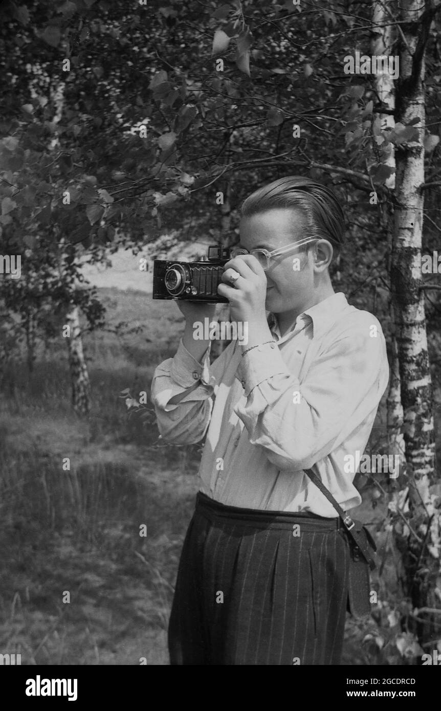 années 1950, historique, à l'extérieur dans une zone boisée, un homme prenant des photos à l'aide d'un appareil-photo à film pliant. Ce type d'appareil photo portable, populaire dans les années 1890, a vu l'objectif et l'obturateur reliés au corps de l'appareil photo par des soufflets pliants légers. Comme nous l'avons vu ici, lorsque l'appareil photo a été déplié, il a fourni la distance de mise au point correcte par rapport au film pour prendre une photo. Banque D'Images