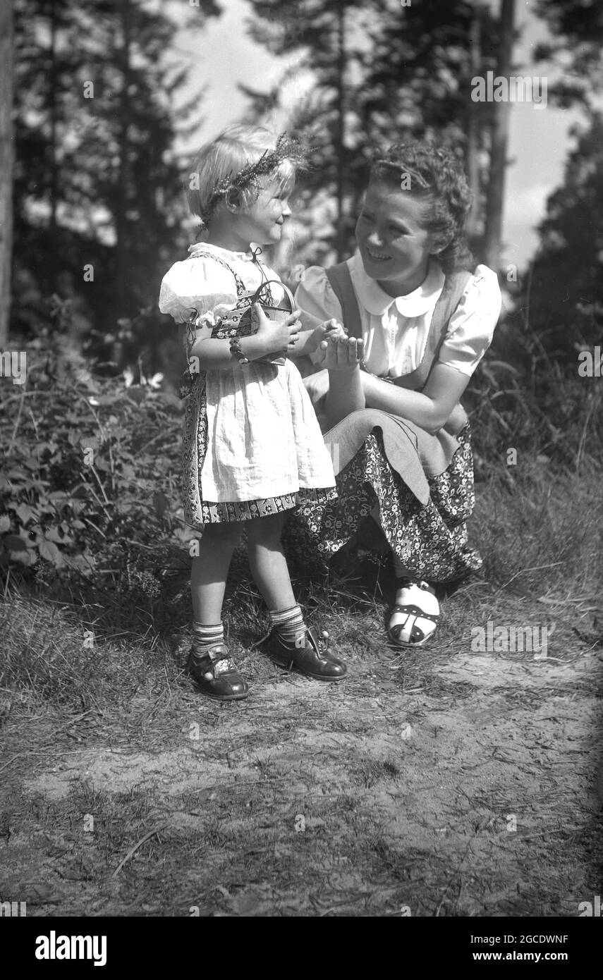 Années 1950, historique, une jeune fille avec sa mère cueillant des fleurs  sauvages dans une forêt, Bavière, Allemagne. Les deux portent une robe  féminine, traditionnellement portée par les femmes et les filles