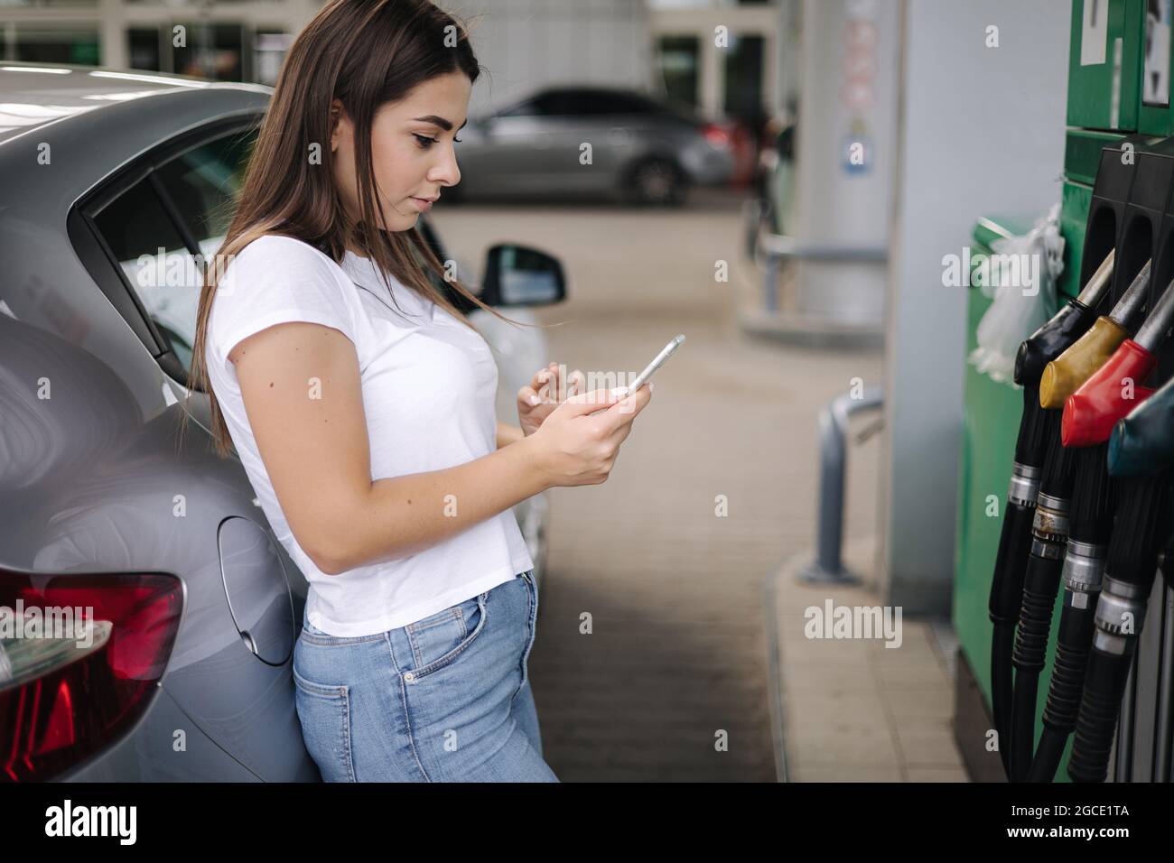 Une jeune femme attirante utilisant son téléphone et se pencha sur sa voiture à la station-service. Femme en attente d'un employé de station-service Banque D'Images
