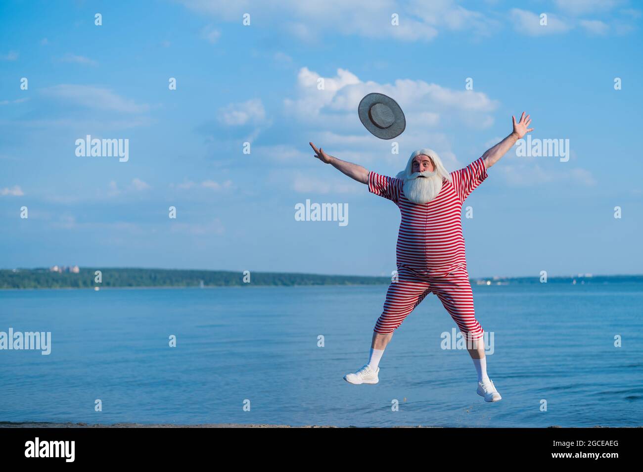 Un homme âgé à barbe dans un costume à rayures classique et un chapeau de plaisancier se promener sur la plage Banque D'Images