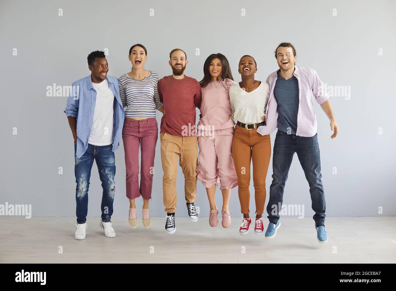 Groupe diversifié de jeunes hommes et femmes heureux excités dans des vêtements décontractés sautant en studio Banque D'Images