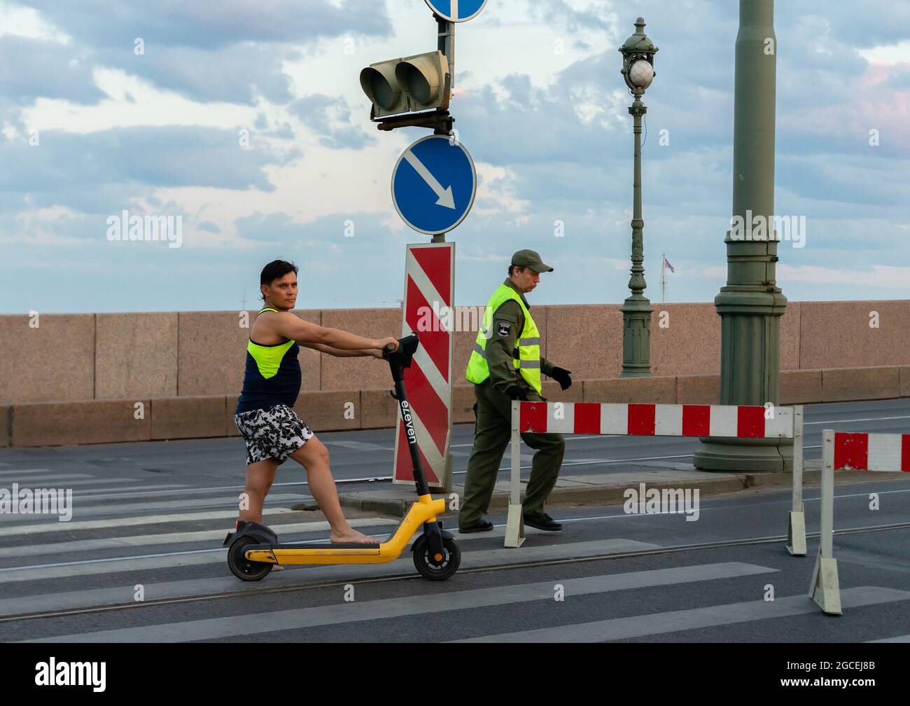 Travailleur routier démontant la barrière de circulation au pont Trinity en début de matinée tandis que l'homme se tient avec son scooter; Saint-Pétersbourg, Russie Banque D'Images