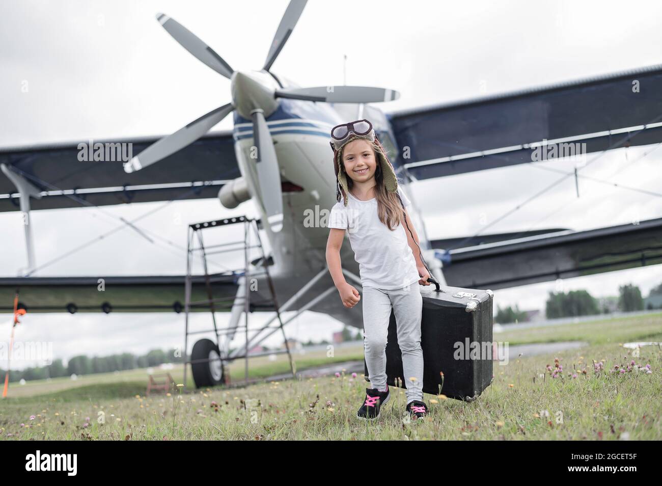 Une petite fille dans le costume d'un pilote porte une valise rétro et  marche le long de l'aérodrome. Un enfant dans un chapeau et des lunettes  est en voyage par avion Photo