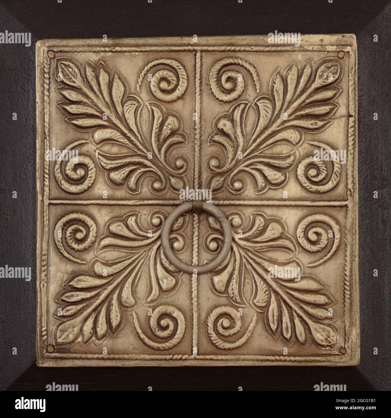 un panneau métallique estampé décoratif carré d'un tiroir en bois foncé avec des motifs botaniques stylisés et une poignée circulaire au centre, dans des tons bruns Banque D'Images