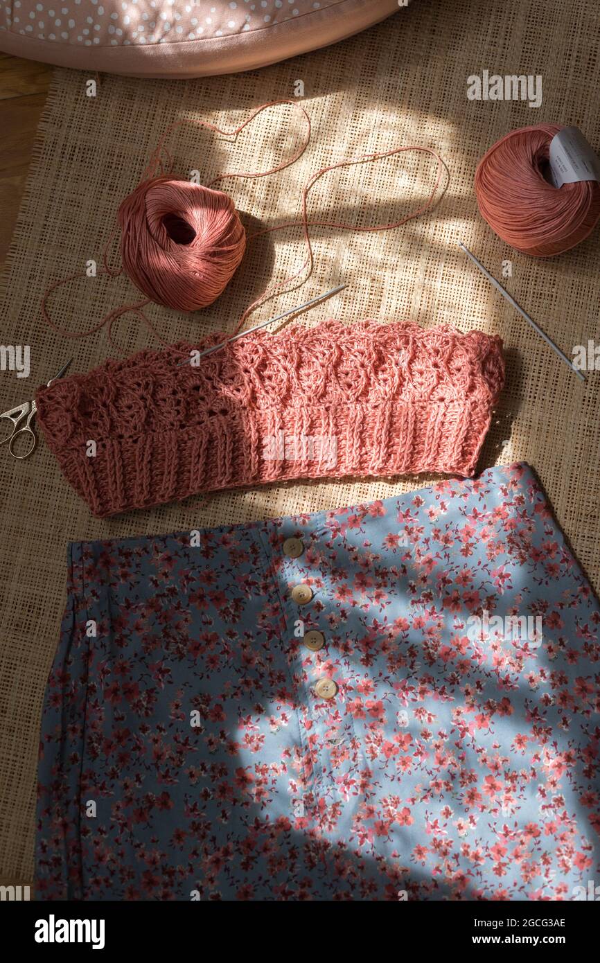 Haut en crochet rose inachevé à côté d'une jupe parfaitement combinée et un couple de fils sur un fond de toile de fond. Banque D'Images