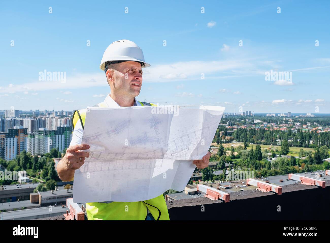 Homme dans un casque blanc tient le plan de construction et inspecte le chantier de construction Banque D'Images