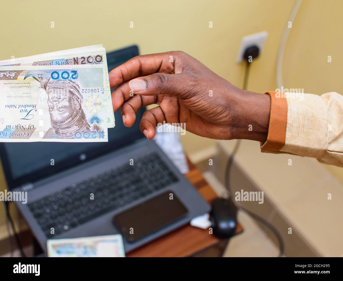 Une main africaine recevant des billets, de l'argent ou de la monnaie nigérians Naira avec un ordinateur portable en arrière-plan Banque D'Images