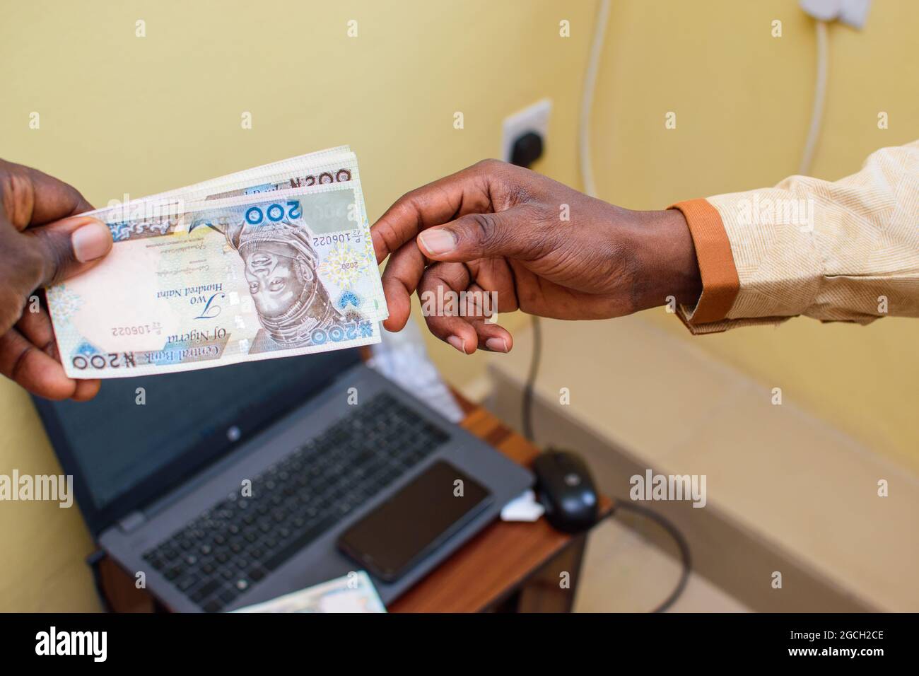 Une main africaine recevant des billets, de l'argent ou de la monnaie nigérians Naira avec un ordinateur portable en arrière-plan Banque D'Images