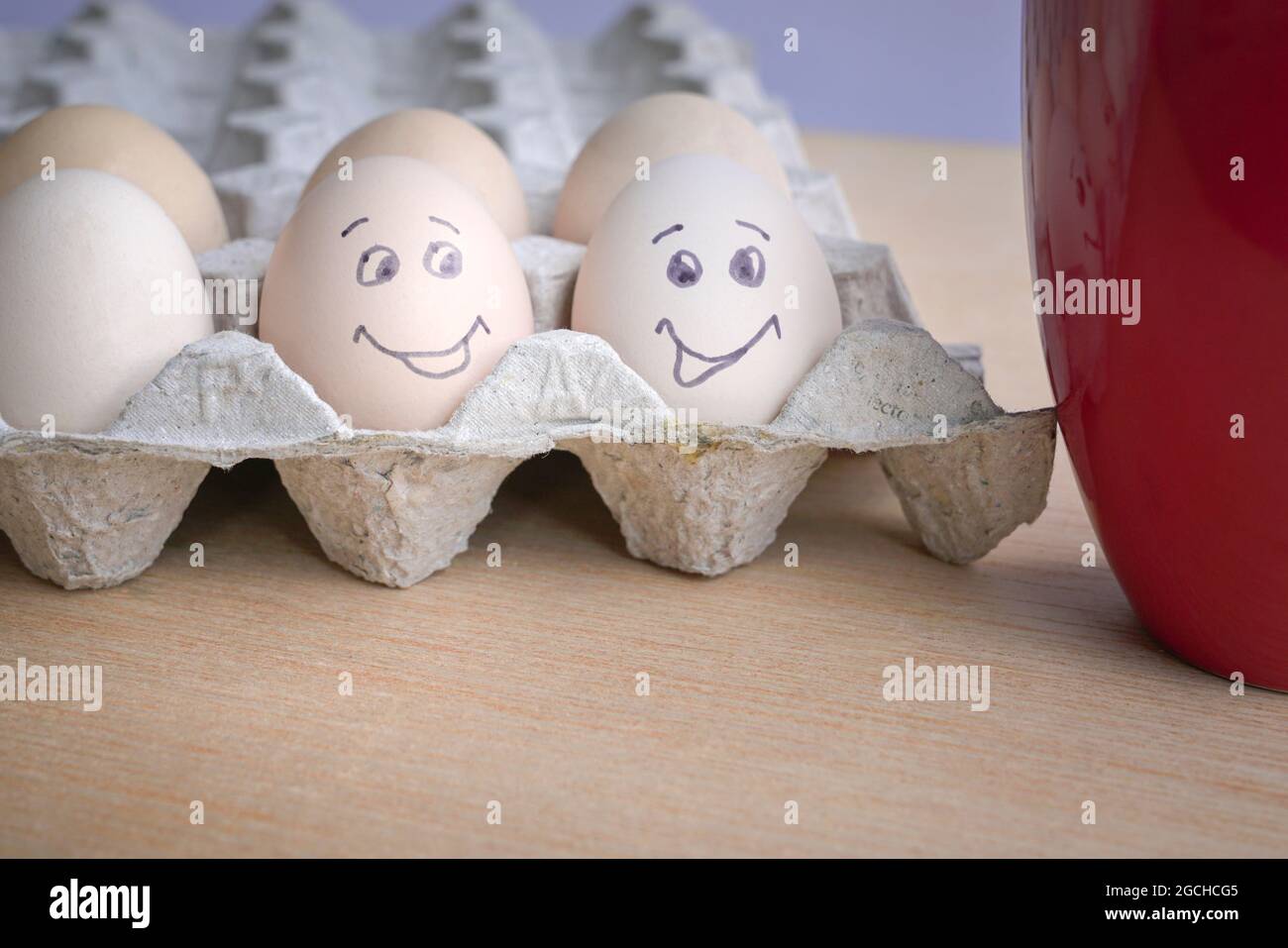 Deux œufs peints avec un visage souriant à côté d'une tasse de café rouge. Concept petit déjeuner bon matin. Banque D'Images