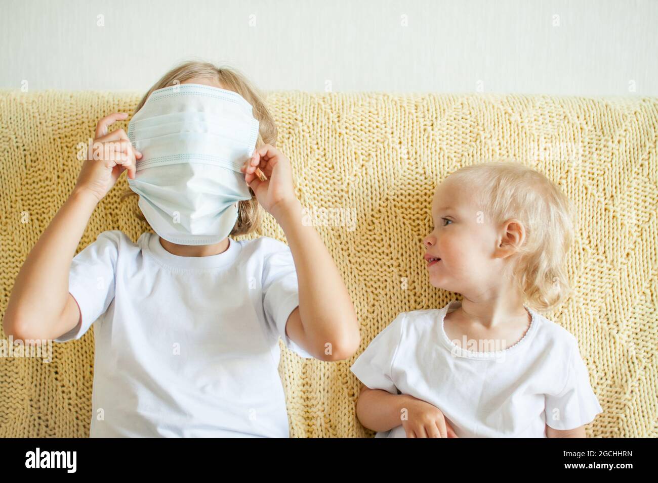 Portrait de deux sœurs portant des masques médicaux de protection. La sœur aînée aide le plus jeune. Sœurs jouant du plaisir. Concept de protection contre les coronavirus Banque D'Images