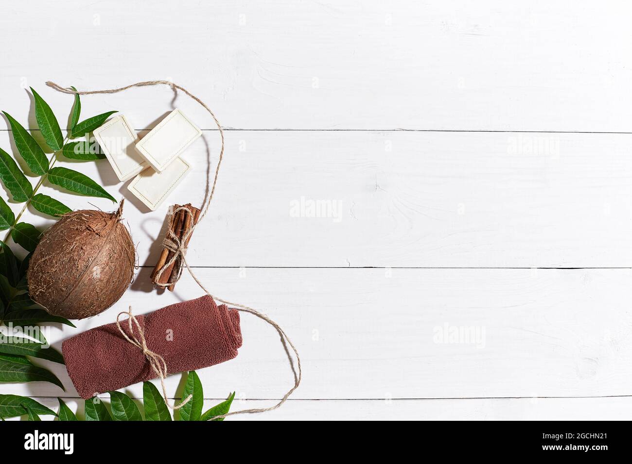 Savons naturels faits à la main avec cannelle, serviette brune, noix de coco et feuilles vertes sur fond de bois blanc Banque D'Images