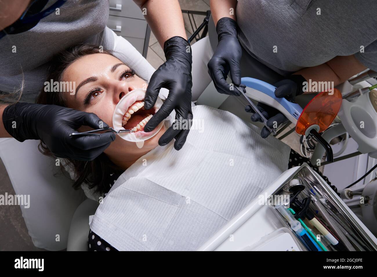 Belle femme en chaise dentaire pendant la procédure d'installation des bretelles aux dents supérieure et inférieure. Dentiste et assistant travaillant ensemble, outils dentaires i Banque D'Images