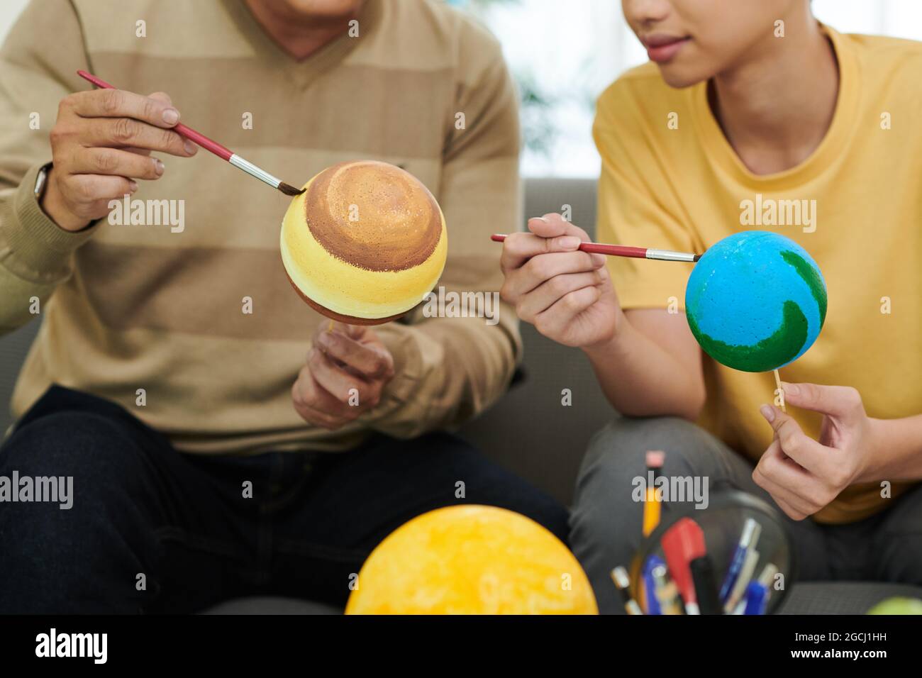 Père et fils peignant des boules en plastique lors de la fabrication du modèle de système solaire pour l'école Banque D'Images