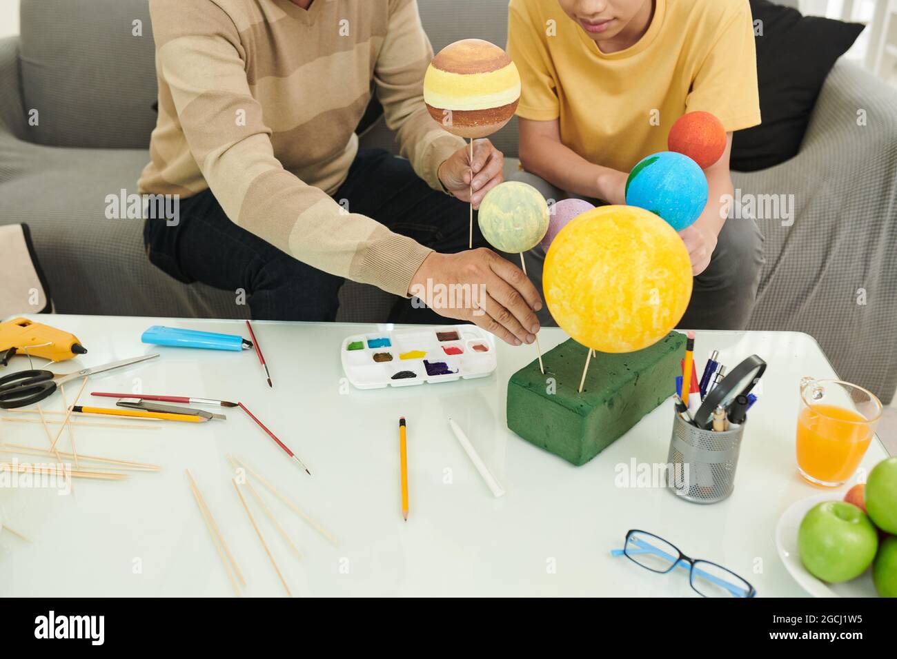 Père et fils mettant des pointes dans des planètes en styromousse lors de la peinture pour le projet du système solaire Banque D'Images