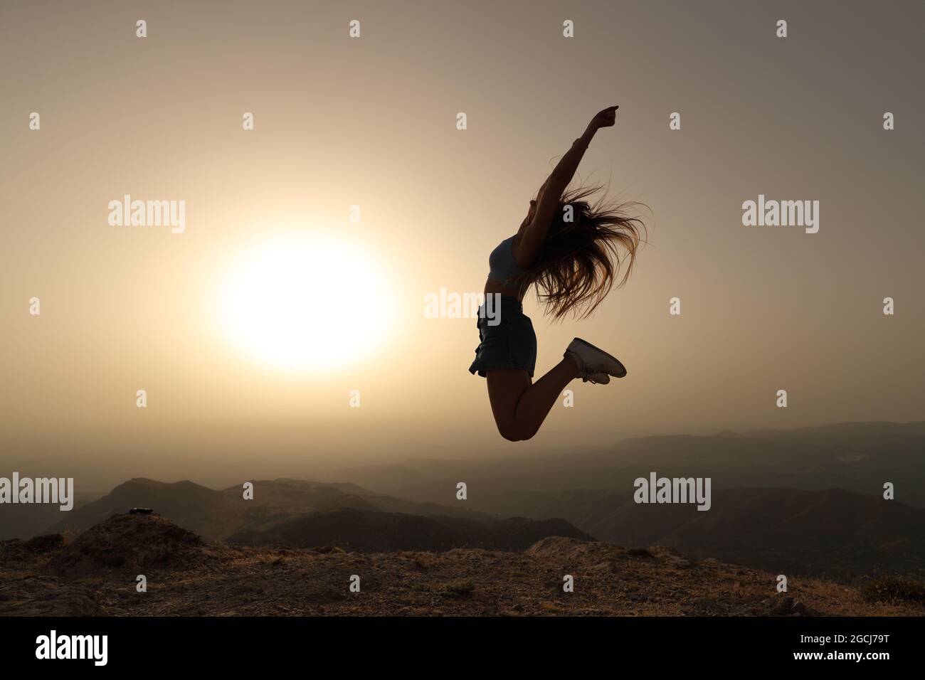 Vue latérale d'une silhouette de femme sautant au coucher du soleil dans la montagne Banque D'Images