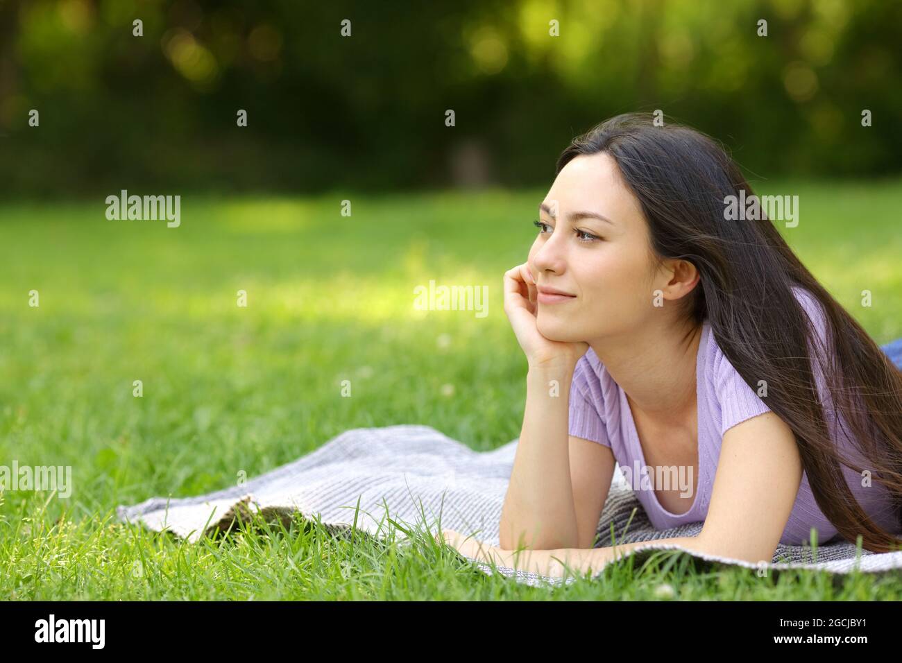 Femme de race mixte contemplant et pensant allongé sur l'herbe dans un parc Banque D'Images