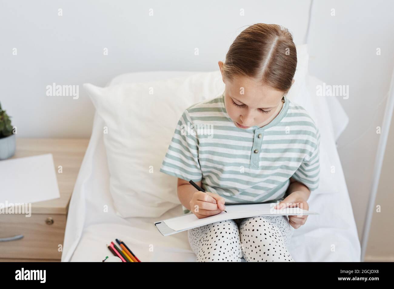 Portrait minimal d'une petite fille dans la chambre d'hôpital, dessin de photos tout en étant assis sur le lit, espace de copie Banque D'Images