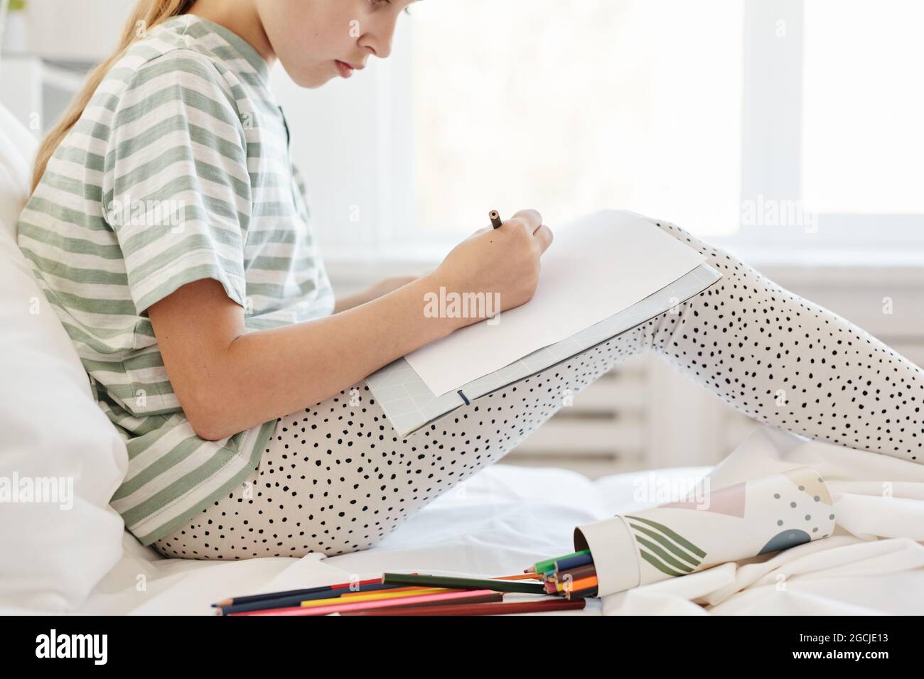 Mini vue latérale portrait de petite fille assise sur le lit et dessin dans la pièce blanche, espace de copie Banque D'Images