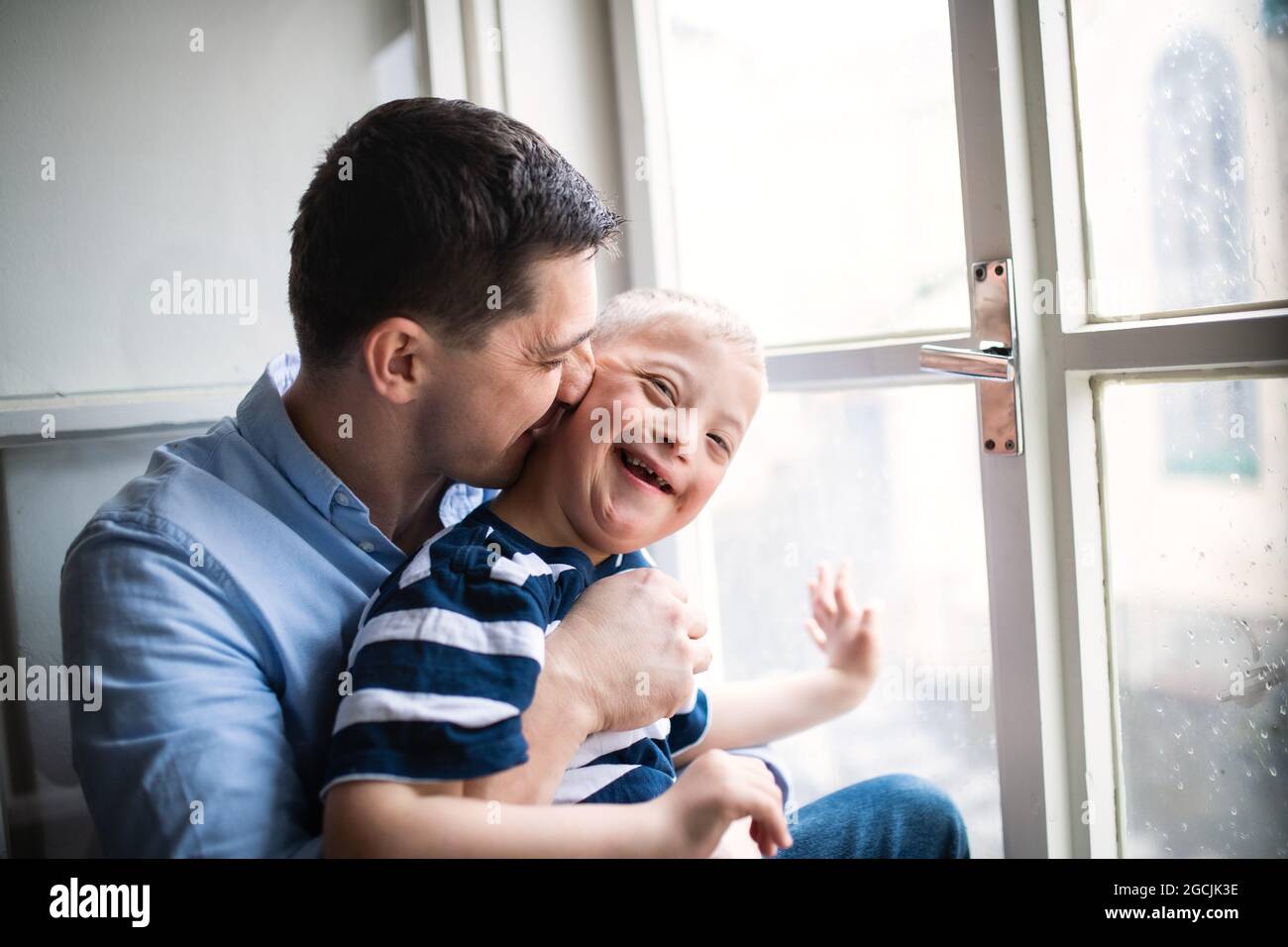 Père avec le syndrome de Happy Down fils à l'intérieur à la maison, embrassant sa joue. Banque D'Images