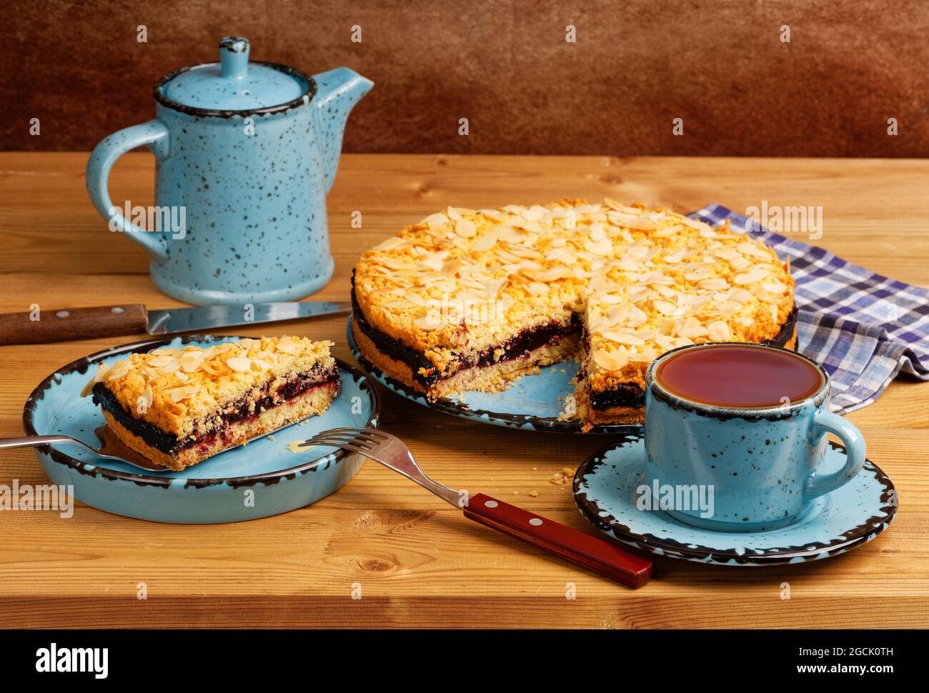 Gâteau maison au cassis décoré de pétales d'amande et d'une tasse de thé sur une table en bois. Banque D'Images Gâteau maison au cassis décoré de pétales d'amande et d'une tasse de thé sur une table en bois. Banque D'Images