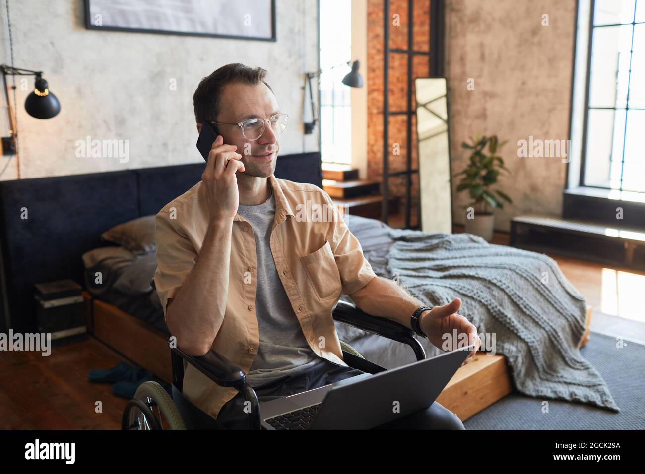 Portrait d'un homme adulte moderne avec un handicap parlant au smartphone tout en travaillant de la maison dans un intérieur design, espace de copie Banque D'Images