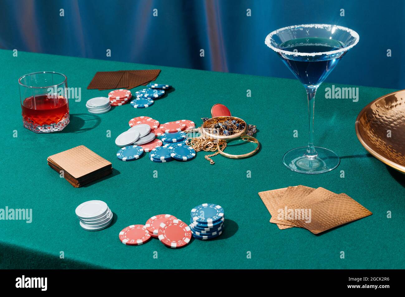 Table de poker verte avec des cartes et des jetons placés près des bijoux et des verres avec des cocktails alcoolisés Banque D'Images