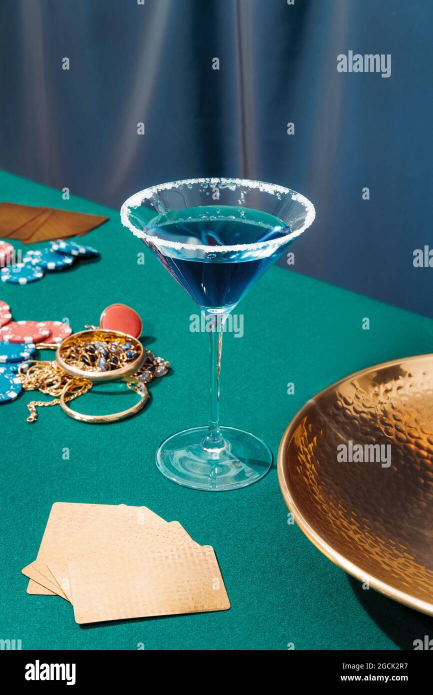 Table de poker verte avec des cartes et des jetons placés près des bijoux et des verres avec des cocktails alcoolisés Banque D'Images