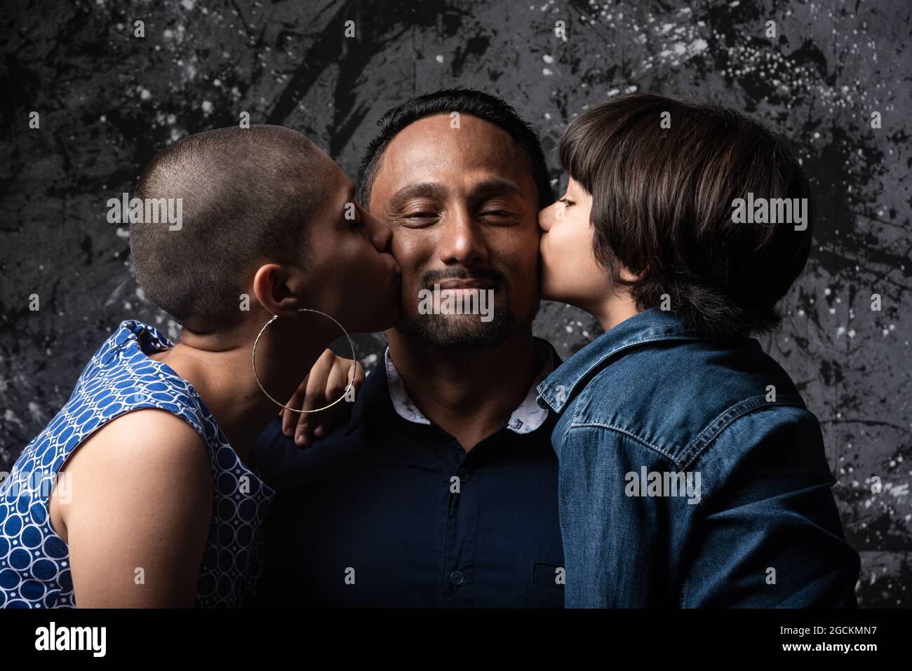 Femme aimante multiethnique et fils adolescent embrassant homme sur joue sur fond sombre en studio Banque D'Images