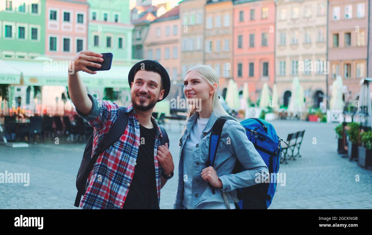 Couple de touristes faisant selfie sur smartphone dans le centre-ville. Ils ont des sacs de touristes. Banque D'Images