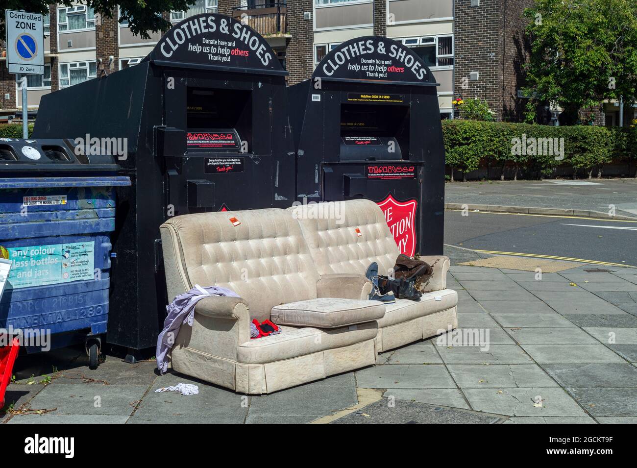 Vieux canapé et les vêtements jetés dans la rue par Bins, Portsmouth City, Hampshire, Royaume-Uni Banque D'Images