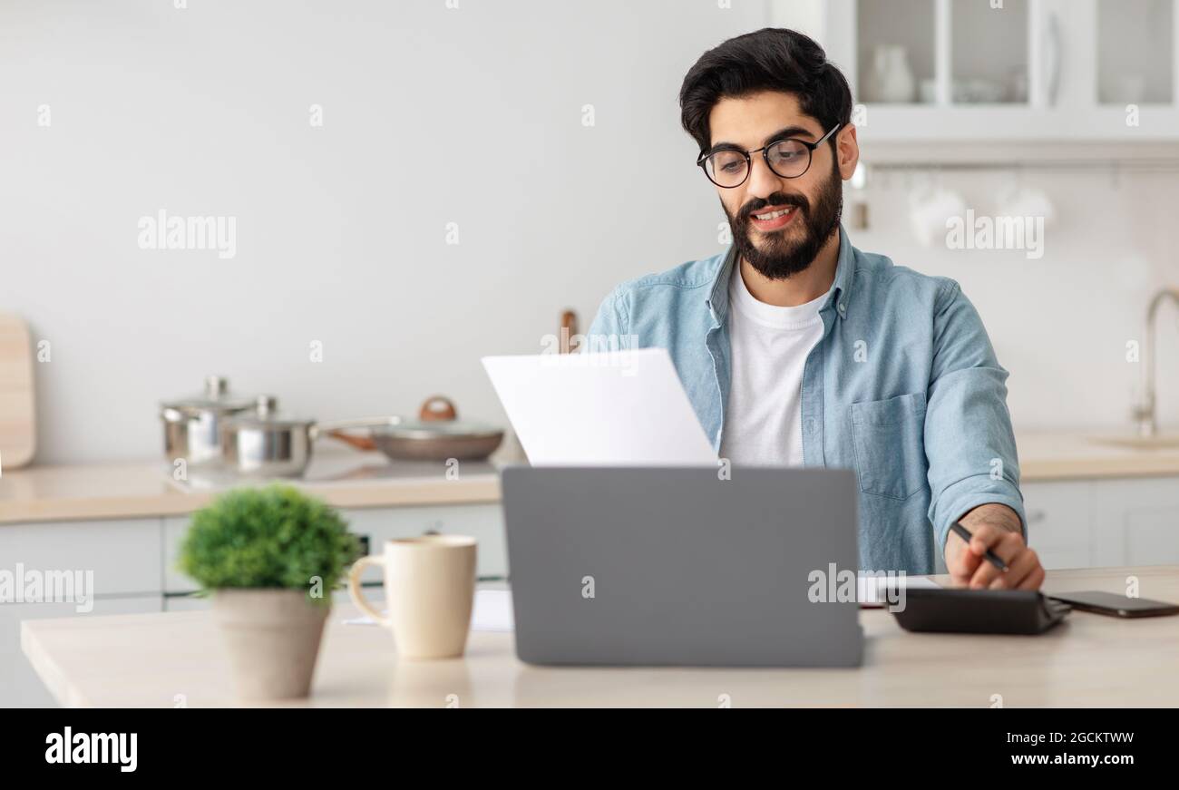 Portrait d'un homme arabe heureux lisant des documents d'assurance à la maison, assis à table dans la cuisine et comptant le budget de la maison Banque D'Images