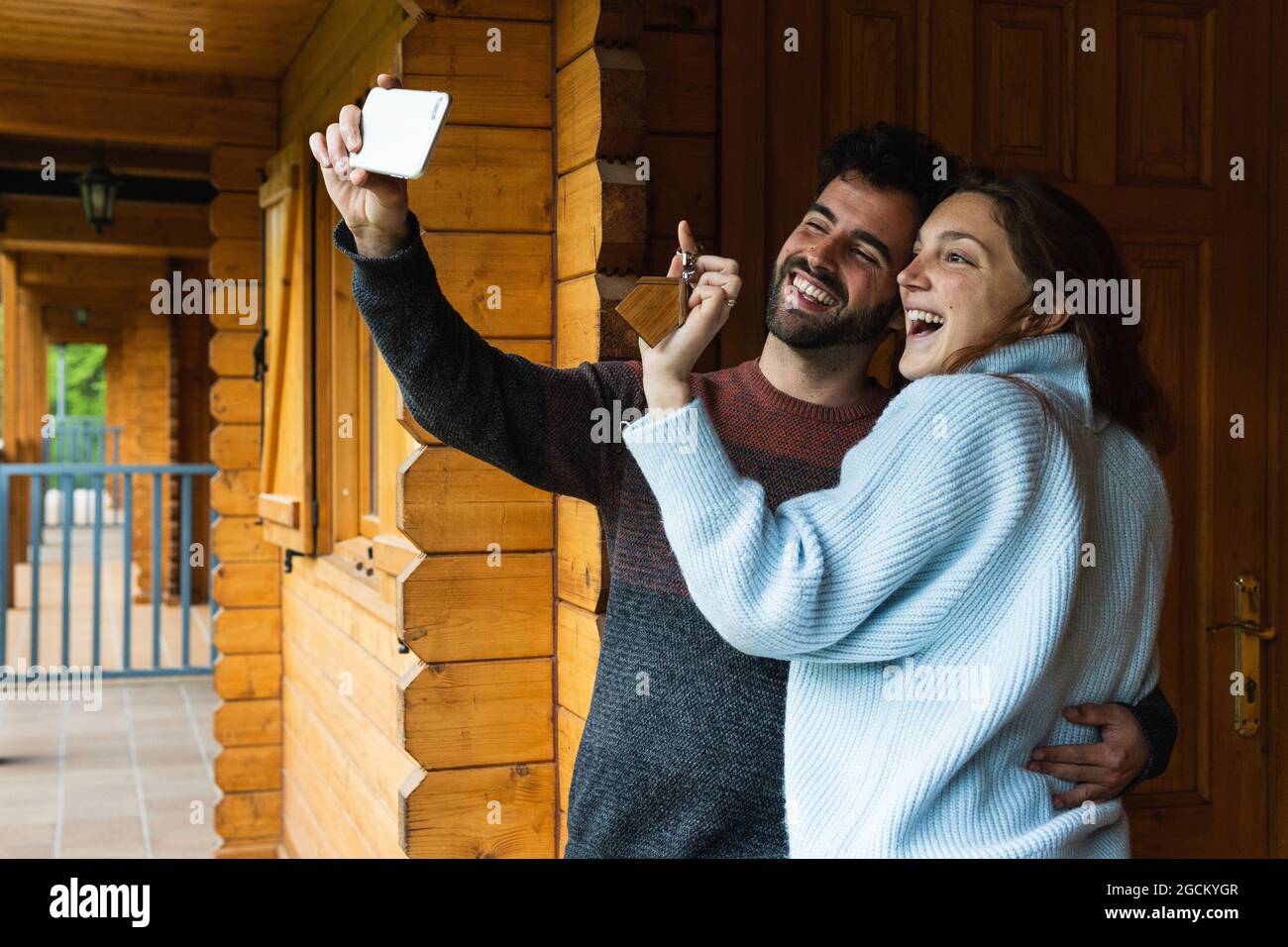 Couple gai avec les clés d'un nouveau chalet en bois enserre et prend auto-shot sur téléphone mobile dans les Pyrénées Banque D'Images
