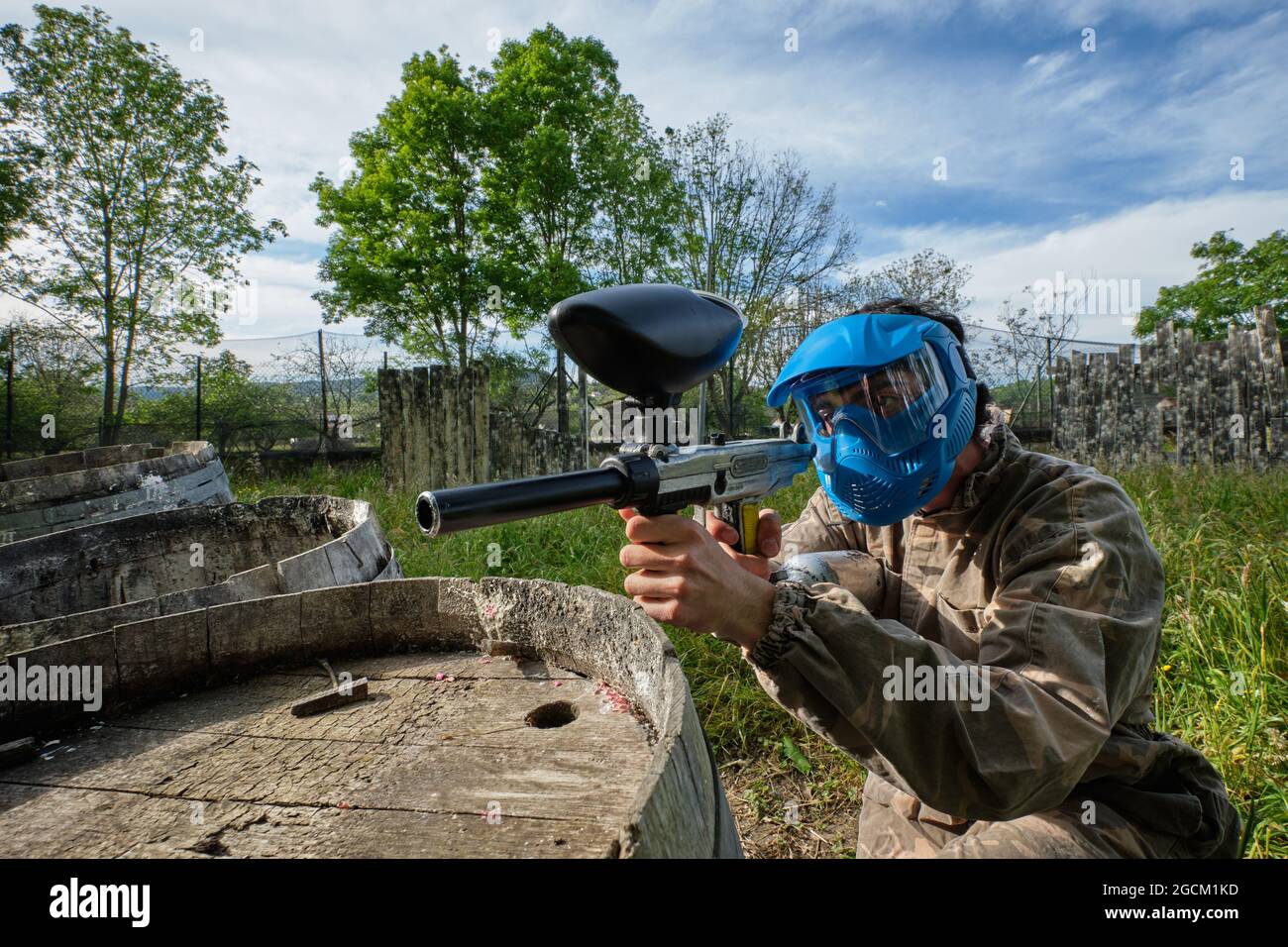 Un joueur masculin en casque et en tenue de camouflage, qui cherche à s'éloigner lors d'un match de paintball en campagne Banque D'Images