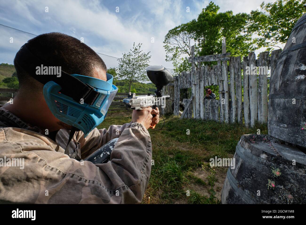 Jeu de tir masculin anonyme avec un pistolet à paintball visant à l'ennemi se cachant derrière un mur en bois pendant le match Banque D'Images