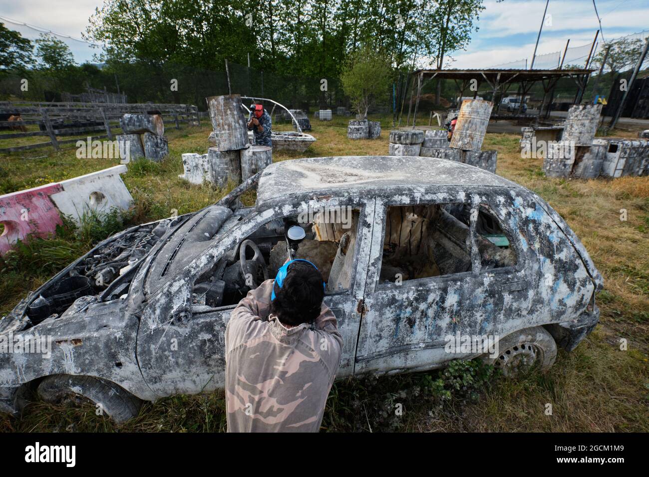 Des hommes méconnaissables avec des armes à feu et dans des casques de protection jouant du paintball parmi les voitures abandonnées Banque D'Images