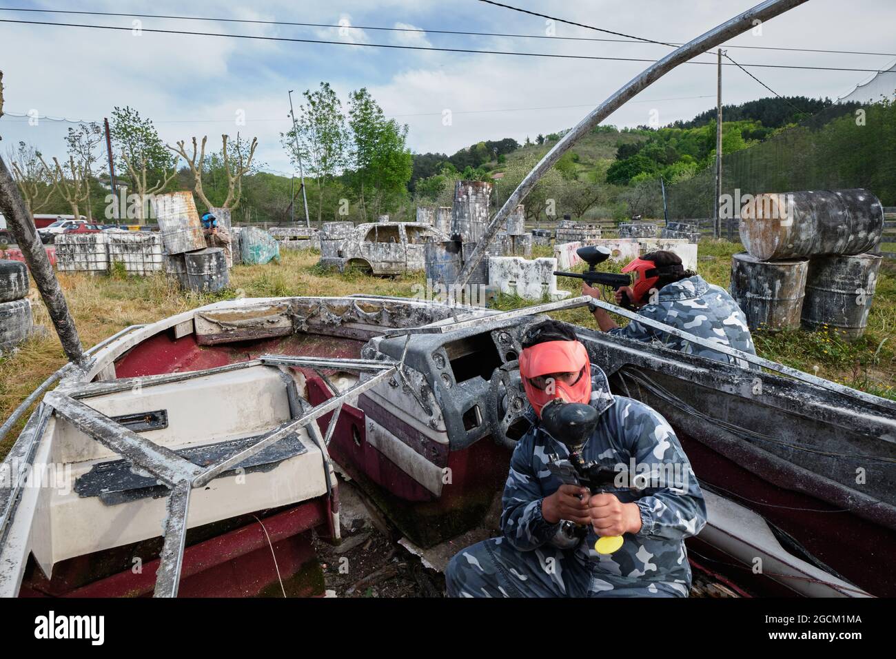 Des hommes méconnaissables avec des armes à feu et dans des casques de protection jouant du paintball parmi les bateaux et les voitures abandonnés Banque D'Images