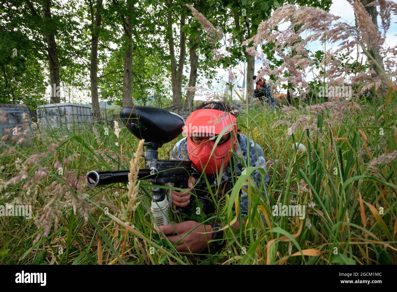 Joueur masculin méconnaissable dans un casque et avec un fusil visant l'équipe adverse tout en jouant au paintball dans la nature Banque D'Images
