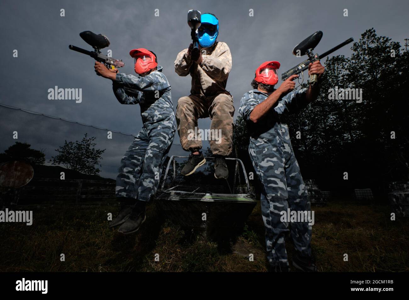 Faible angle des équipes de joueurs de paintball en tenue de camouflage et avec des fusils sur fond de ciel nuageux en soirée Banque D'Images