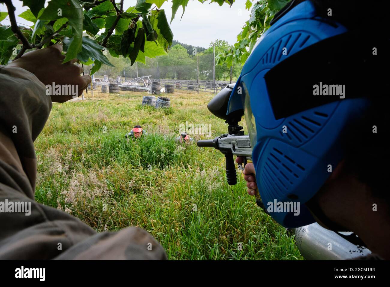 Vue arrière d'un joueur masculin méconnaissable dans un casque et avec un fusil visant l'équipe adverse tout en jouant au paintball dans la nature Banque D'Images