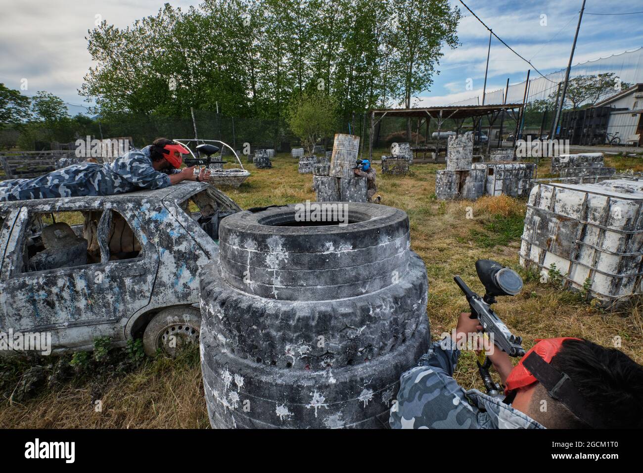 Joueurs masculins méconnaissables en tenue de camouflage jouant paintball parmi les vieux transports abandonnés et les déchets Banque D'Images