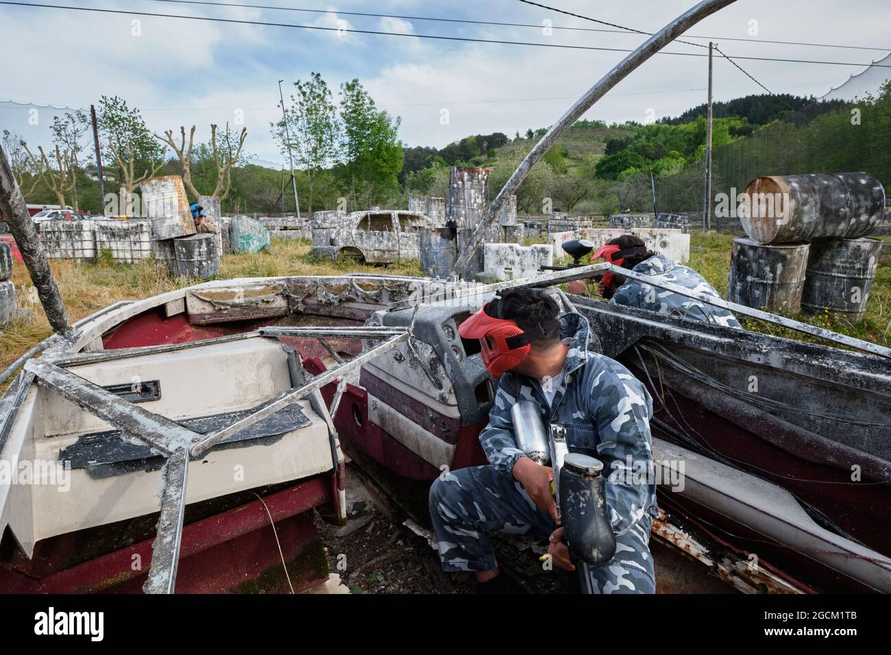 Des hommes méconnaissables avec des armes à feu et dans des casques de protection jouant du paintball parmi les bateaux et les voitures abandonnés Banque D'Images