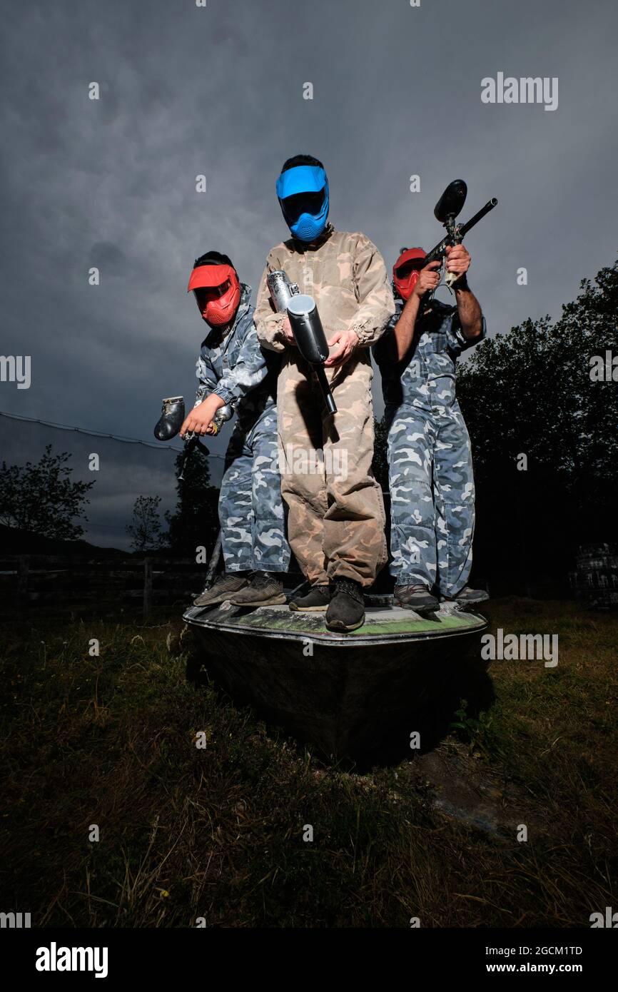 Faible angle des équipes de joueurs de paintball en tenue de camouflage et avec des fusils sur fond de ciel nuageux en soirée Banque D'Images