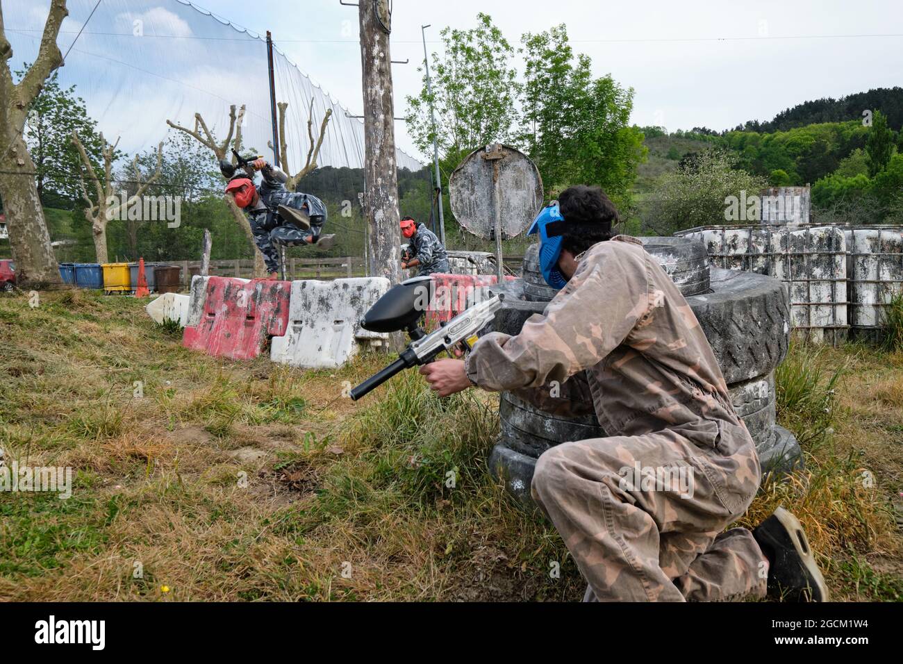 Des hommes actifs dans des casques de protection et des vêtements de camouflage jouant paintball parmi les déchets abandonnés Banque D'Images