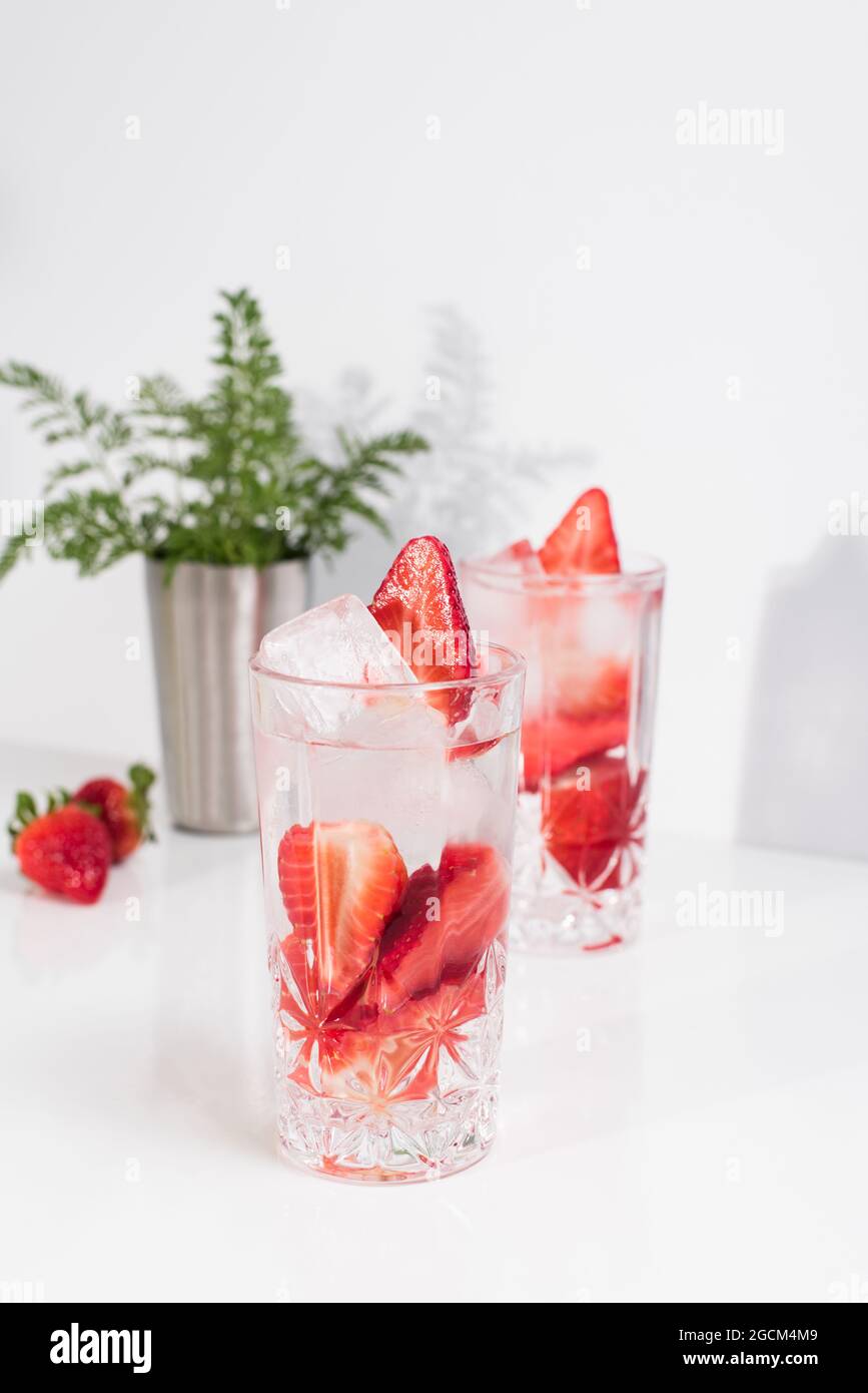 Boisson rafraîchissante d'été avec des fraises fraîches en tranches et des glaçons avec de l'eau servis dans des verres sur une table blanche Banque D'Images