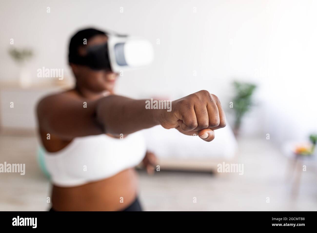 Formation virtuelle. Femme noire en surpoids dans des lunettes VR en utilisant le simulateur de combat, faisant le punch à la maison, se concentrer sur le poing Banque D'Images