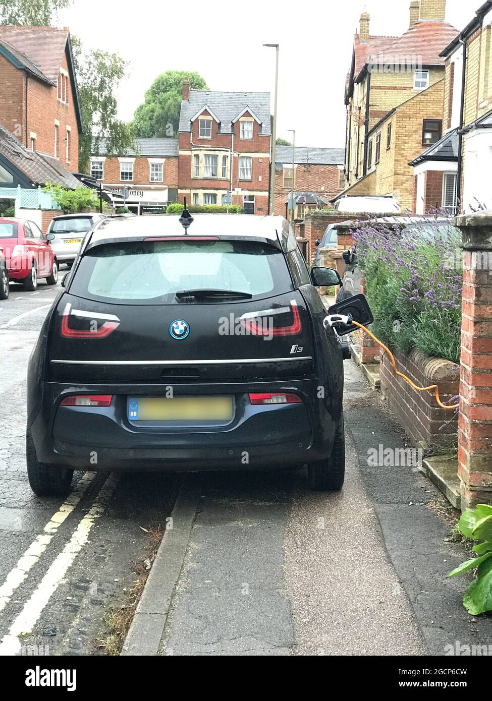 Point de charge !Infrastructure de charge - charge d'une voiture électrique avec un câble suspendu sur la chaussée et stationné sur des lignes jaunes doubles Banque D'Images